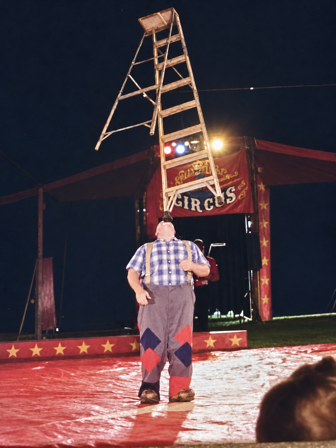 Circus performer balancing a full ladder on his head under the big top at night